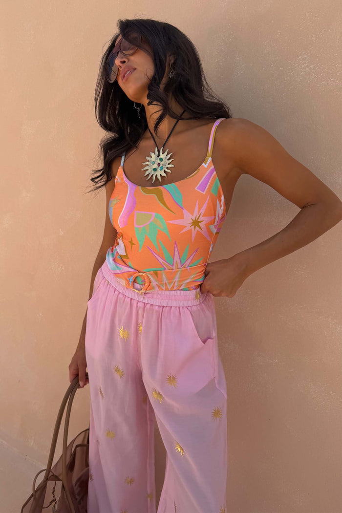 Pink Elissa Trousers with gold foil sun motifs and a wide-leg fit, paired with a patterned top and sun necklace.