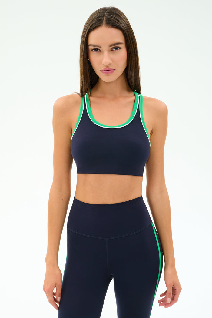 A woman stands against a light background wearing the SPLITS59 Robbie Airweight Bra in Indigo/Spearmint, looking directly at the camera.