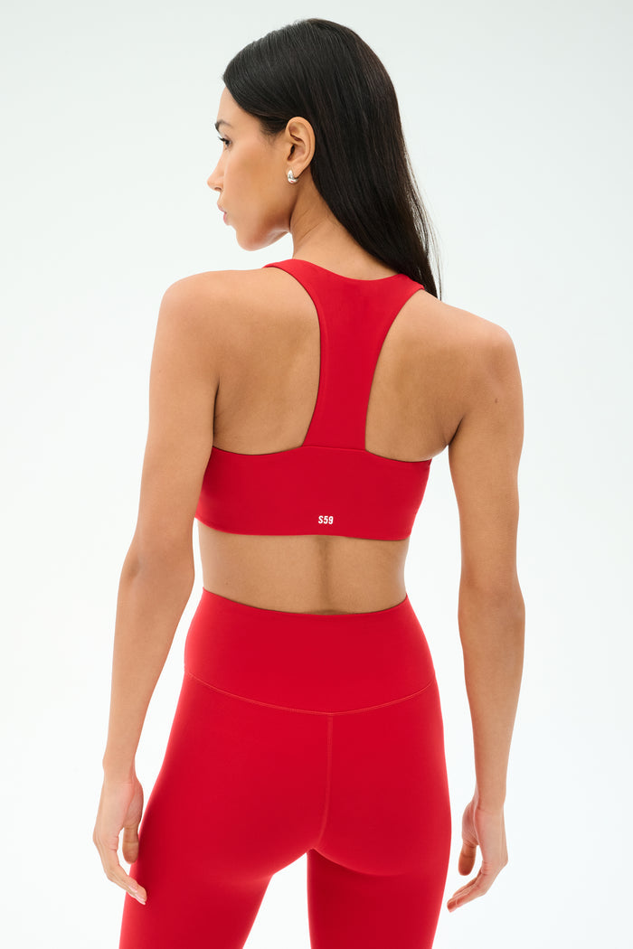 A woman, seen from the back against a light background, wears the SPLITS59 Sara Airweight Bra in Pirate Red with matching leggings—ideal activewear for Pilates or hot yoga.