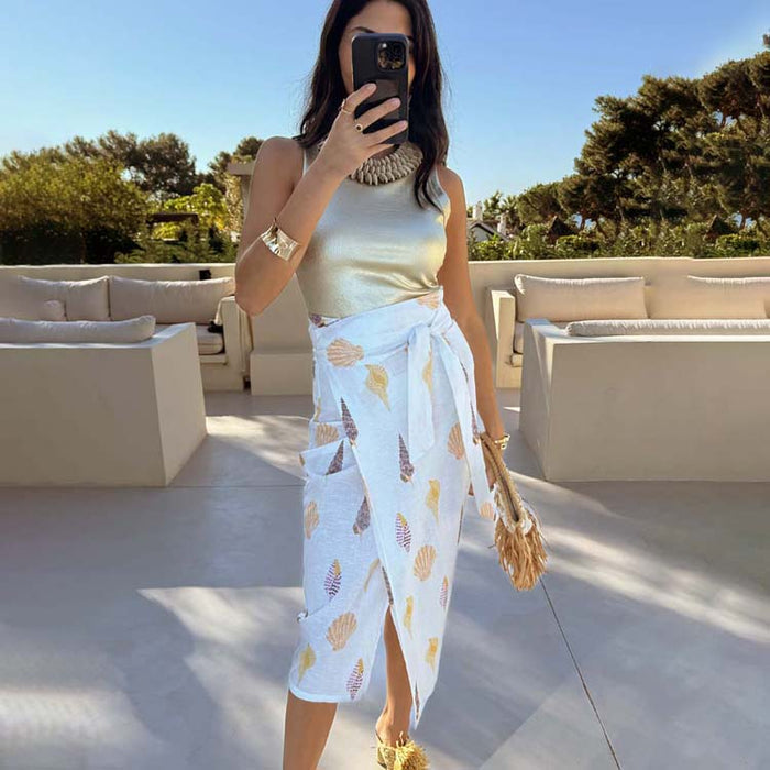 White Shells Jaspre Wrap Skirt with a golden sea shell print, styled with a metallic top for a summer vacation look.