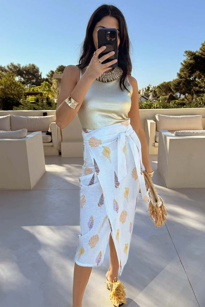 White Shells Jaspre Wrap Skirt featuring a shell print and wrap tie, styled with a gold top for a vacation look.