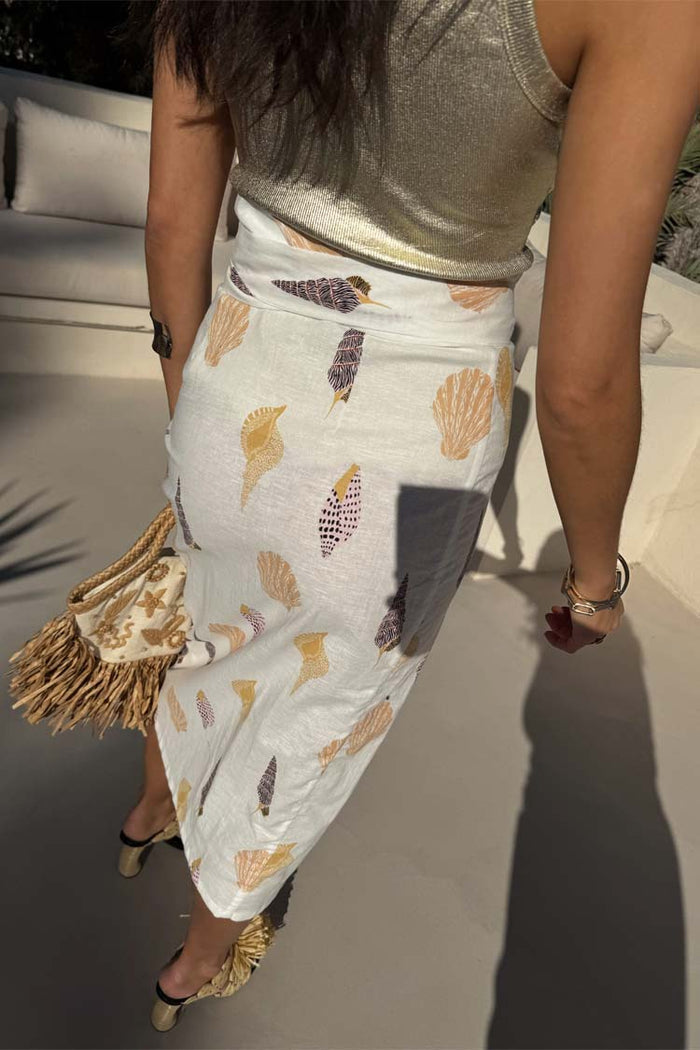 Shells Jaspre Wrap Skirt in white with a golden shell print, paired with a metallic top and straw fringe bag.