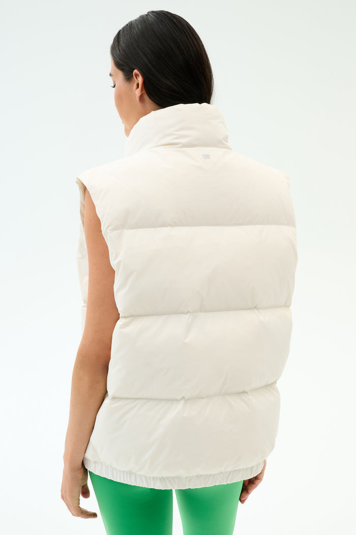 A woman is shown from the back wearing the SPLITS59 Summit Nylon Puffer Vest in white and green pants against a plain background—an ideal lightweight layer for cool weather workouts.