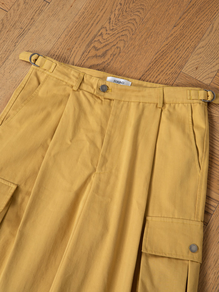 A close-up of FOUND Sunlight Twill Cargo Shorts—unisex, mustard yellow with pleats and flap pockets—laid flat on a wooden floor.