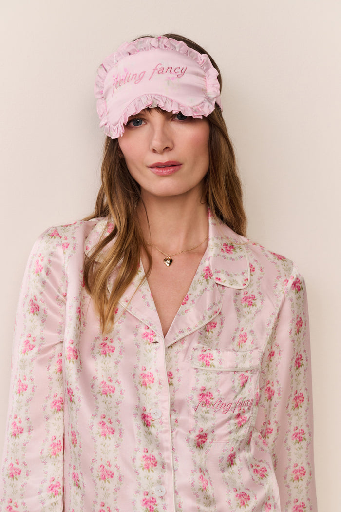Woman wearing a pink floral pajama set and matching sleep mask with 'feeling fancy' text.