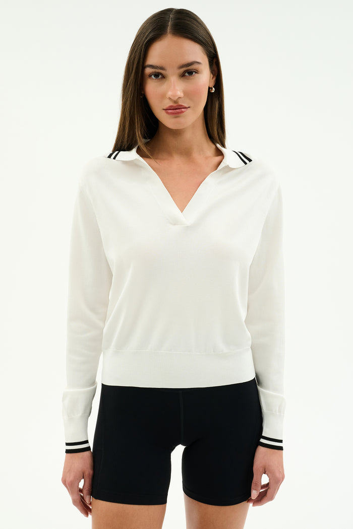 A woman stands against a plain white background wearing the SPLITS59 Taylor Knit Polo in white with black trim and black shorts.