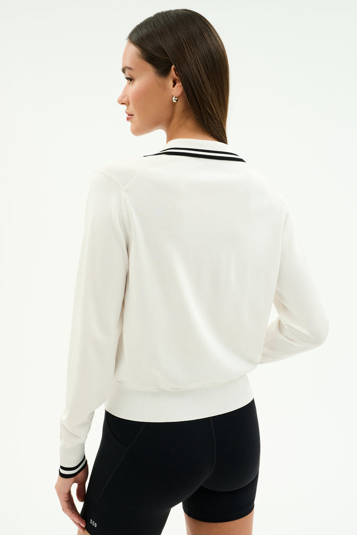 A woman with straight brown hair wears the SPLITS59 Taylor Knit Polo in white/black, paired with black shorts, standing with her back to the camera against a plain background.
