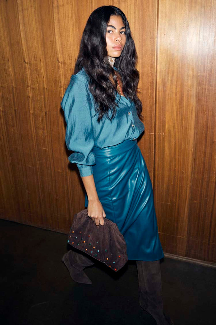 Teal Vegan Leather Jaspre Skirt styled with a matching teal shirt and a brown studded clutch.