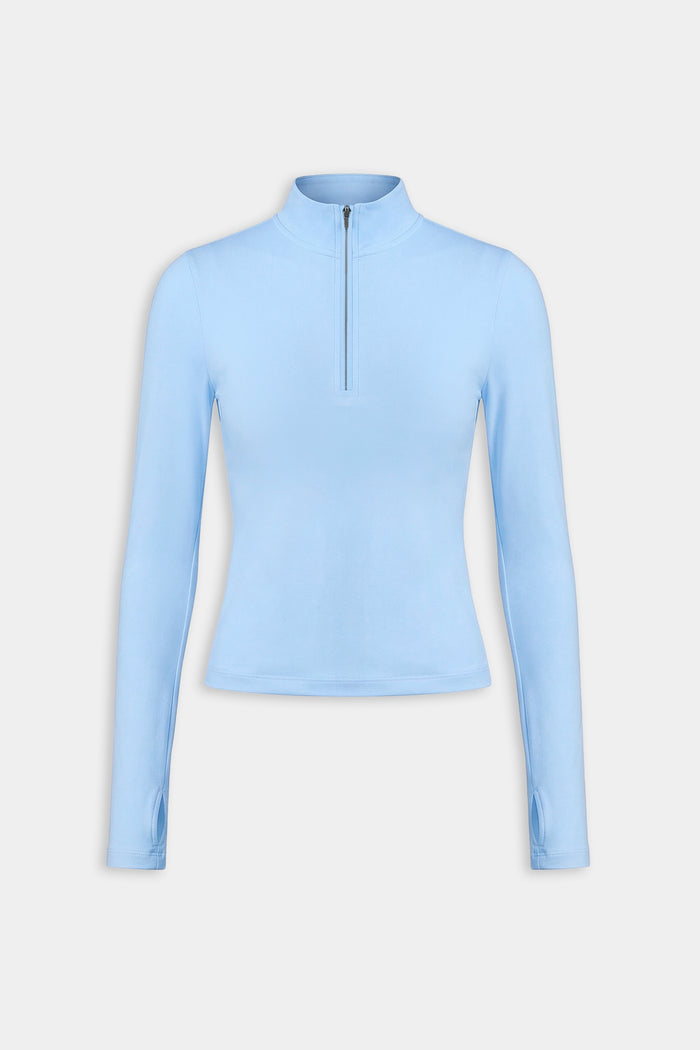 The SPLITS59 Tess Rigor Half Zip Waist Length in Skylight is a women's light blue long-sleeve top with a mock neck and front half-zip, made from a soft nylon-spandex blend, shown against a plain white background.
