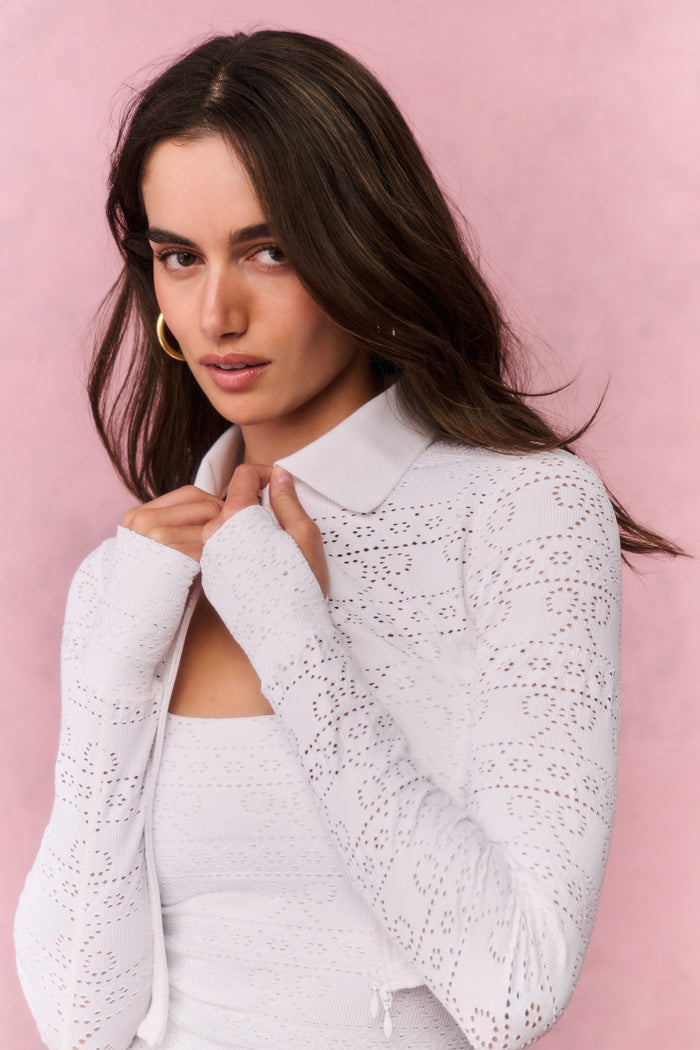 Woman wearing a white lace top and pleated skirt against a pink background