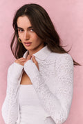 Woman wearing a white lace top and pleated skirt against a pink background