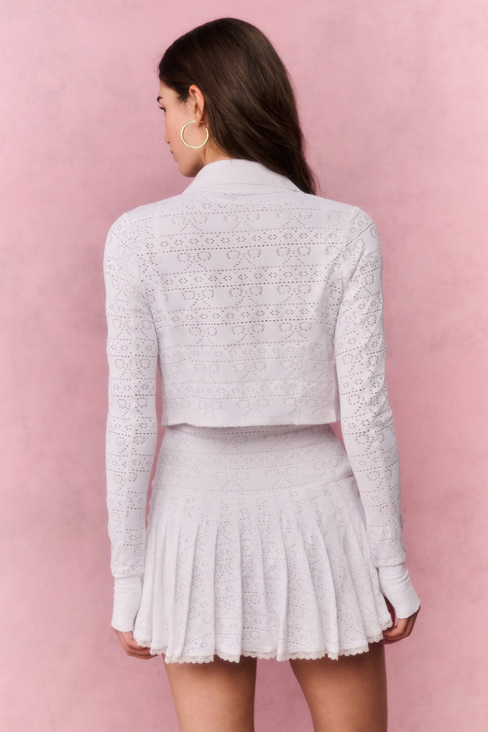 Woman wearing a white lace top and pleated skirt against a pink background