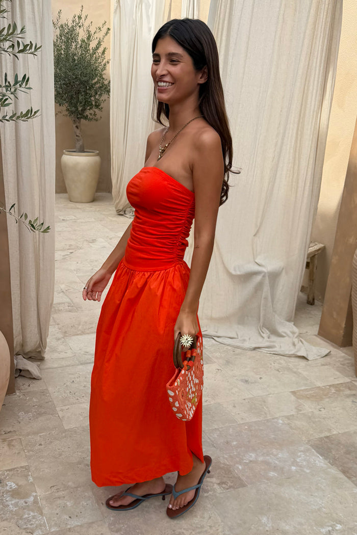 Tomato Lola Mid-axi Dress in red with a ruched strapless bodice and cotton skirt, styled for a vacation look.