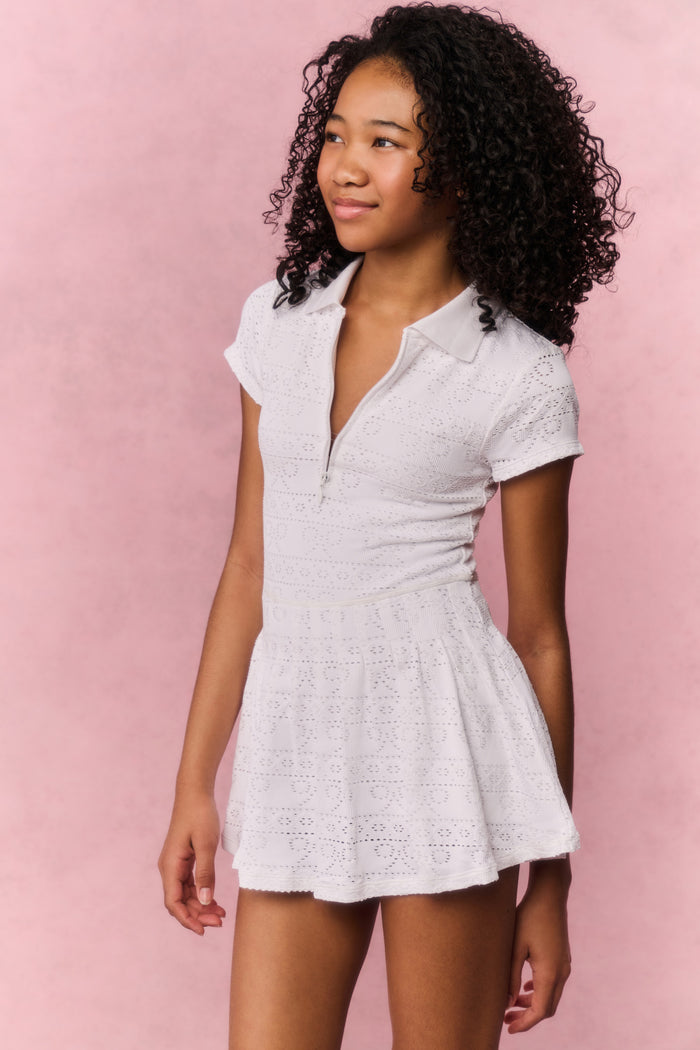 Girl in a white tennis dress against a pink background