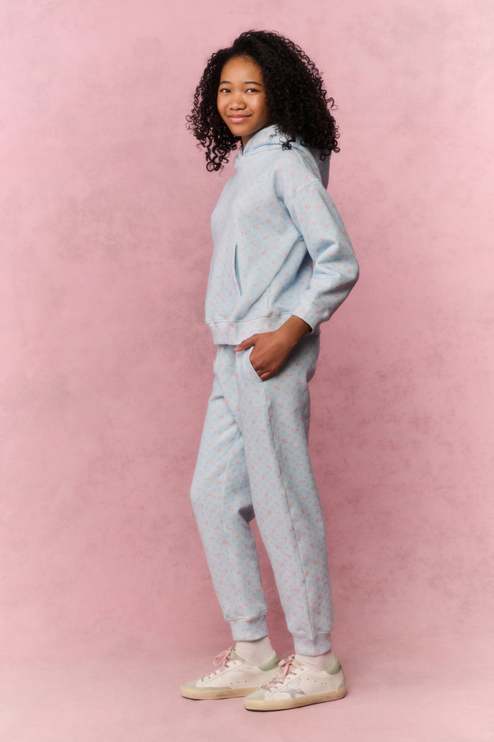 Young girl wearing a blue sweatshirt and pants on a pink background