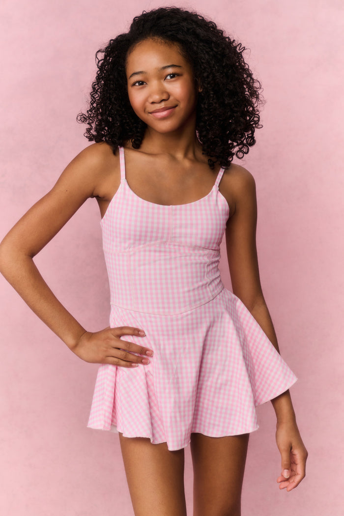 Young girl wearing a pink checkered dress against a pink background