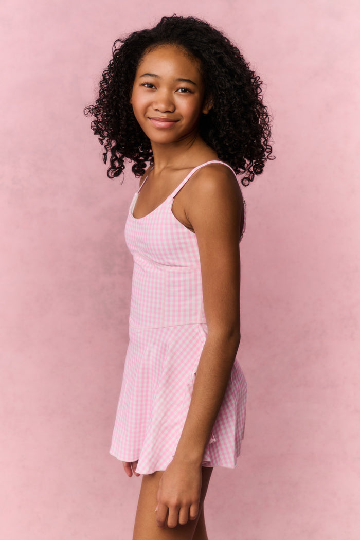 Young girl wearing a pink checkered dress against a pink background