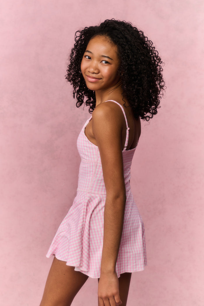 Young girl wearing a pink checkered dress against a pink background