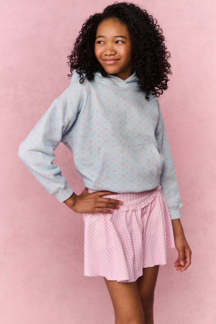 Young girl wearing a light blue hoodie with small patterns and a pink pleated skirt on a pink background