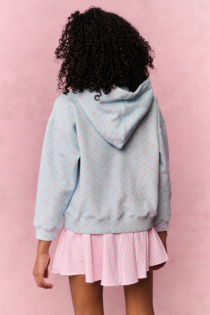 Person wearing a light blue hoodie with small patterns and a pink pleated skirt on a pink background