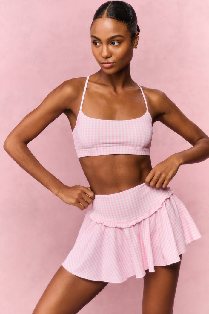 Woman wearing a pink gingham sports bra and skirt outfit against a pink background