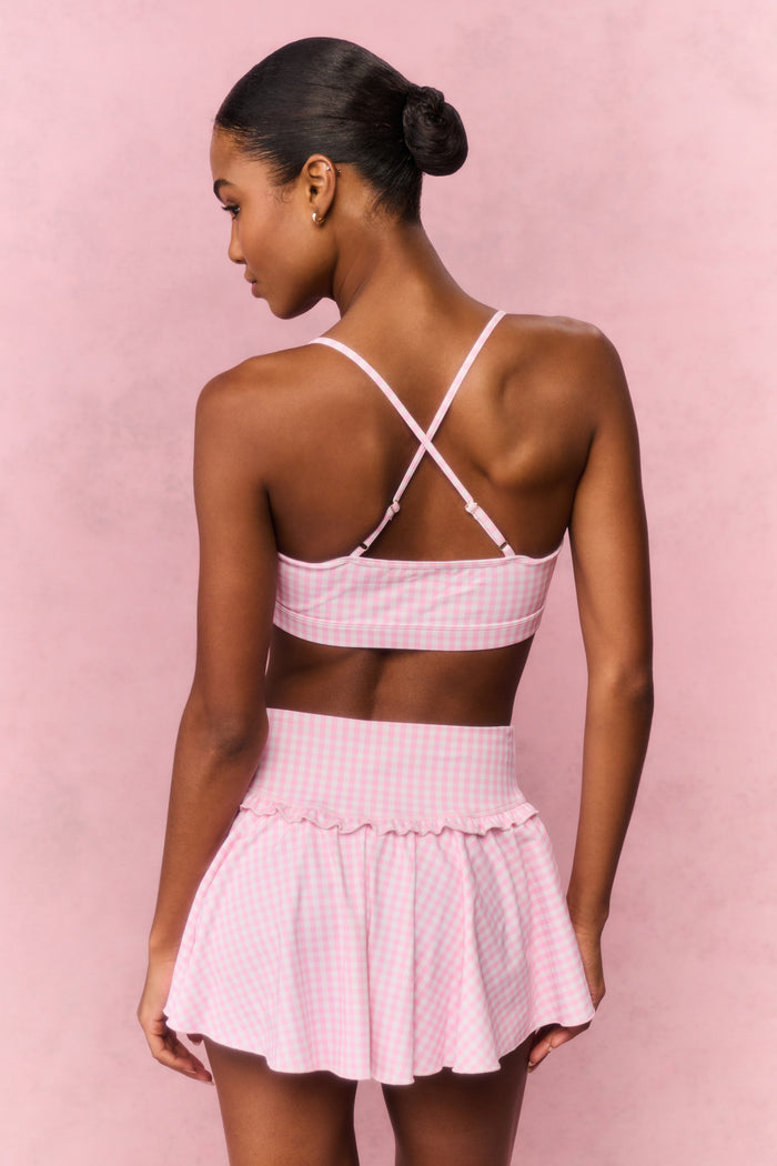 Woman wearing a pink gingham sports bra and skirt outfit against a pink background