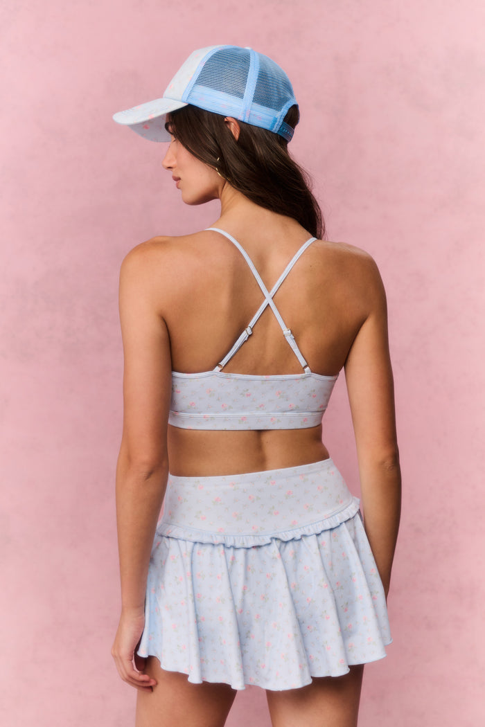 Woman wearing a light blue sports bra and skirt set with a cap on a pink background