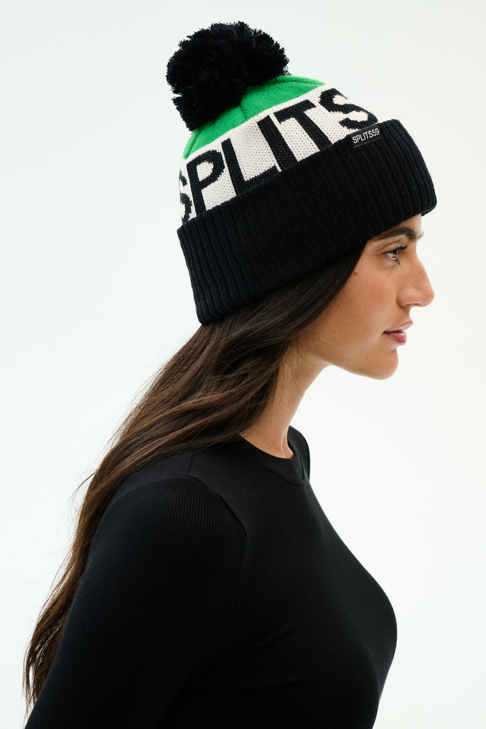 A person wearing a black long-sleeve top and a knit beanie with a black pom-pom and the word "SPLITS" in large white letters.