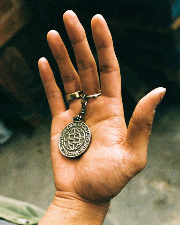 WORLD LOGO METAL KEYCHAIN - silver metal logo keychain, detail in hand - Cold Culture